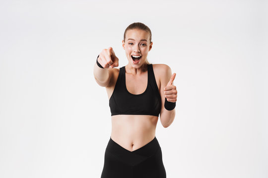 Image of nice amazed woman wearing tracksuit pointing finger at camera and showing thumb up