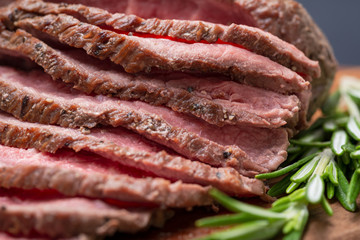 Sliced Grass Fed juicy Corn Roast Beef garnished with Rosemary Fresh Herb on natural wood cutting board.