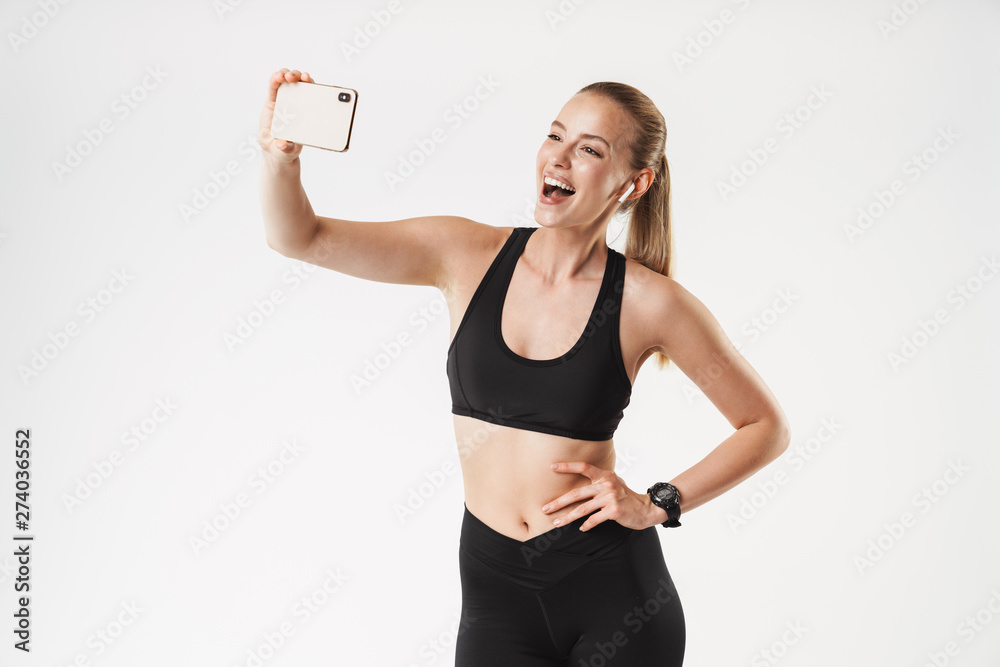 Sticker Image of sporty young woman wearing tracksuit taking selfie photo on cellphone and using earpods