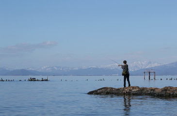 晴天の琵琶湖岸で釣りをする若者