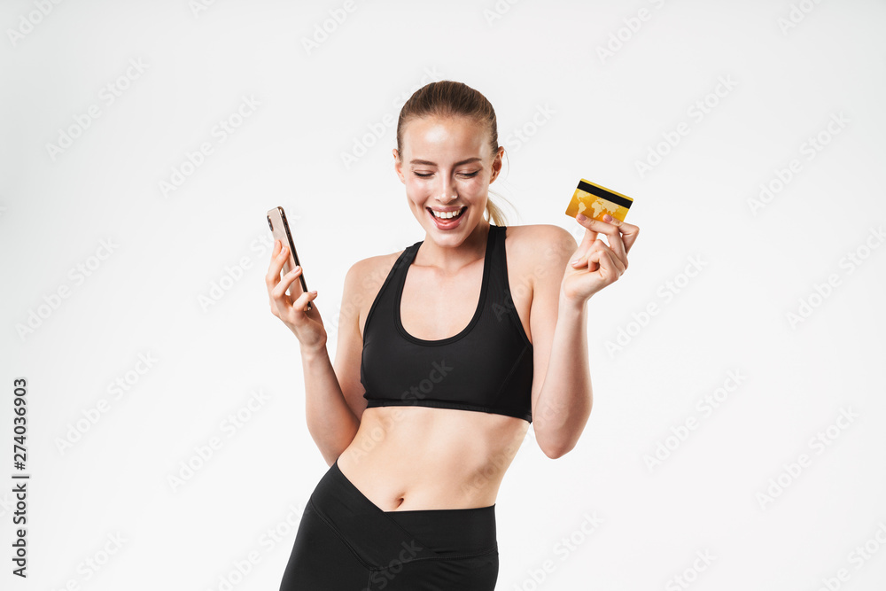 Sticker Image of delighted sporty woman wearing tracksuit rejoicing while holding credit card and cellphone