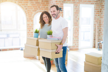 Fototapeta na wymiar Middle age senior couple moving to a new house, holding cardboard boxing smiling happy in love with apartmant