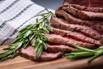 Sliced Grass Fed juicy Corn Roast Beef garnished with Rosemary Fresh Herb on natural wood cutting board.