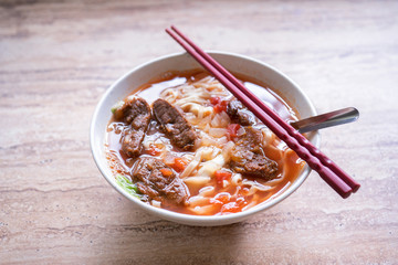Beef noodle ramen meal with tomato sauce broth in bowl on bright wooden table, famous chinese style food in Taiwan, close up, top view, copy space