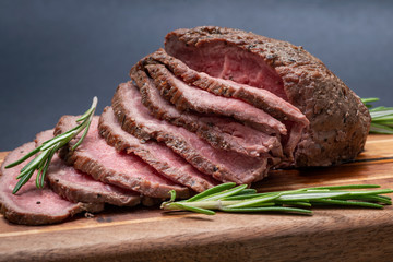 Sliced Grass Fed juicy Corn Roast Beef garnished with Rosemary Fresh Herb on natural wood cutting board.