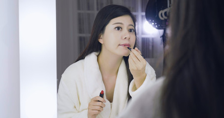 Perfect joyful young woman celebrity in bathrobe sitting in backstage applying lipstick on lips...