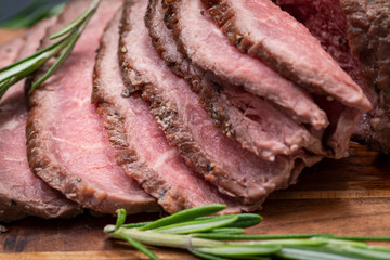 Sliced Grass Fed juicy Corn Roast Beef garnished with Rosemary Fresh Herb on natural wood cutting board.