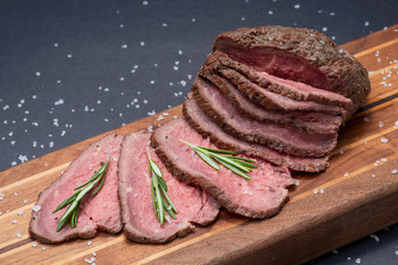 Sliced Grass Fed juicy Corn Roast Beef garnished with Rosemary Fresh Herb on natural wood cutting board.