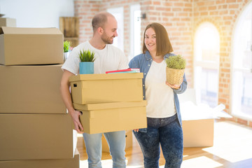 Young couple moving to a new home, smiling happy holding cardboard boxes