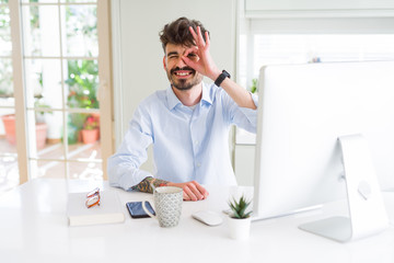 Young business man working using computer doing ok gesture with hand smiling, eye looking through fingers with happy face.