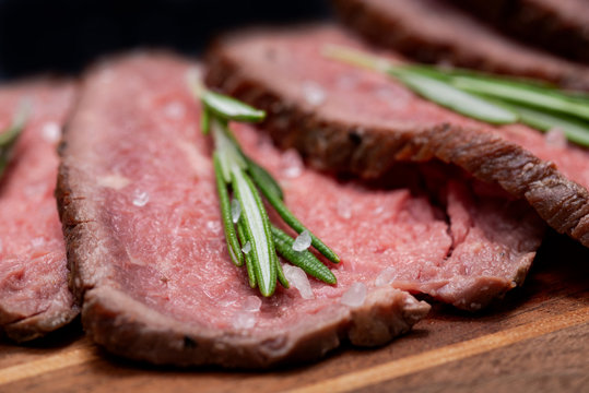 Sliced Grass Fed Juicy Corn Roast Beef Garnished With Rosemary Fresh Herb On Natural Wood Cutting Board.