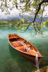 scenic view on beautiful wooden flat rowing boat on lake bled beside attached to a tree, slovenia, go green concept