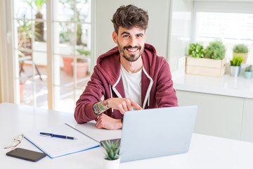 Fototapeta premium Young student man using computer laptop and notebook very happy pointing with hand and finger