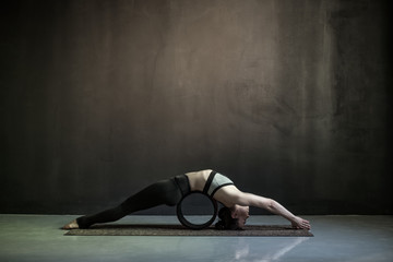 Young caucasian woman practices yoga asana Matsyasana fish pose variation using wheel props. Studio...