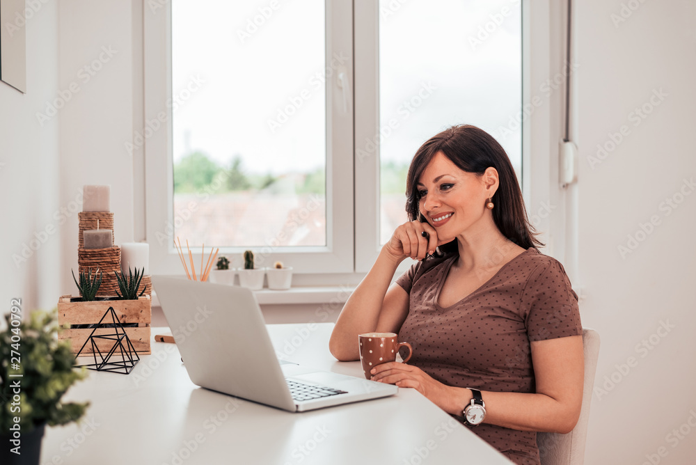 Wall mural portrait of a beautiful woman enjoying morning coffee and looking at laptop.