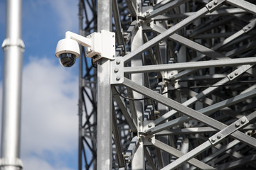 Naklejka premium View of a contemporary surveillance video cam attached to a metal girder of the facade of a modern business skyscraper; security video camera on the frontage of an office high-rise 