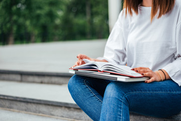 Education concept. Female student sitting on the stairs with notebook and laptop in lap, close-up.