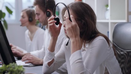 Bored attractive female operator working online listening a conversation of a ccustomer with headset at office, ends the talk, puts off the headset and sighs with a relief. Exhausted, bad mood - Powered by Adobe