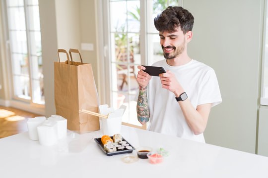 Young man taking pictures with smartphone of sushi asian food from take away delivery