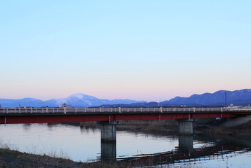 滋賀県彦根市の宇曽川と赤い橋から見える雪化粧の伊吹山とマジックアワーの風景