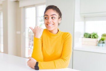 Beautiful young african american woman with afro hair smiling with happy face looking and pointing to the side with thumb up.