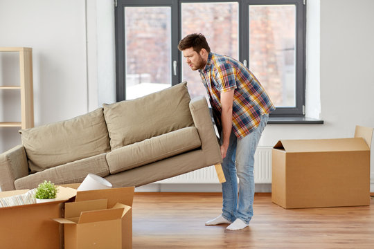 moving, people and real estate concept - man dragging sofa at new home