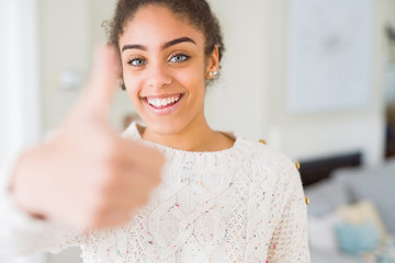 Beautiful young african american woman with afro hair wearing casual sweater doing happy thumbs up gesture with hand. Approving expression looking at the camera showing success.