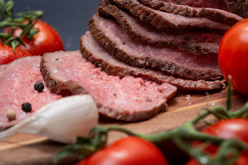 Sliced Grass Fed juicy Corn Roast Beef garnished with Tomatoes, Garlic and Rainbow Peppercorns on natural wooden cutting board.