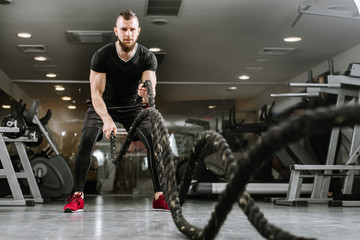 Fototapeta na wymiar Athletic man with battle rope doing exercise in the gym
