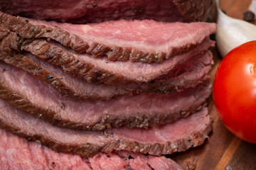 Slices of Grass Fed Corn Roast Beef garnished with Tomatoes and Garlic on natural wooden cutting board.