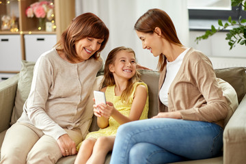 family, generation and technology concept - happy mother, daughter and grandmother with smartphone...