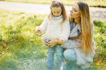 young blonde mother kneeling and hugginb the girl toddler in the park on a sunny day
