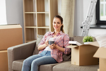 people, repair and real estate concept - smiling woman with stuff moving to new home and drinking coffee