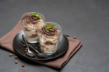 Classic tiramisu dessert in a glass on dark concrete background