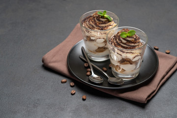 Classic tiramisu dessert in a glass on dark concrete background