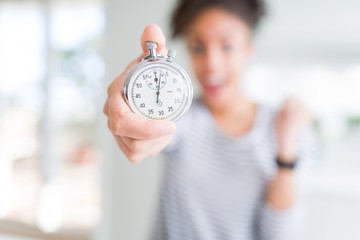 Young african american woman holding stopwatch screaming proud and celebrating victory and success...