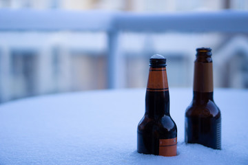 Two bottles of ice cold beer chilling in the snow on a patio table in the middle of winter 