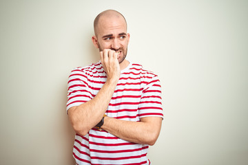 Young bald man with beard wearing casual striped red t-shirt over white isolated background looking stressed and nervous with hands on mouth biting nails. Anxiety problem.