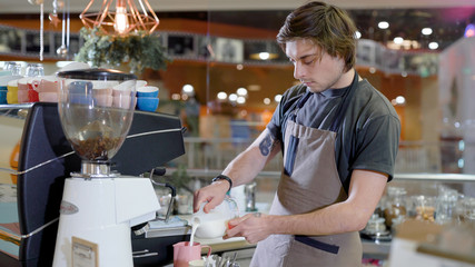 Professional barist standing by the counter and making a coffee.