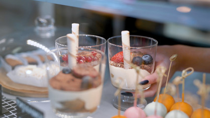 woman is taking sweet desserts with fresh berries in a glasses from candy bar in a kitchen of restaurant