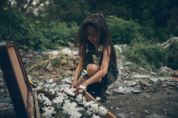 A homeless girl is planting flowers in a suitcase on a garbage dump.