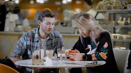 Portrait of a lovely couple in cafe, boyfriend and girlfriend on a date in cozy cafe eating desserts and drinking coffee.