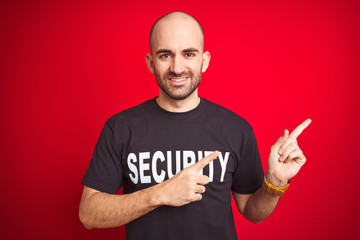 Young safeguard man wearing security uniform over red isolated background smiling and looking at the camera pointing with two hands and fingers to the side.