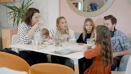 Big group of friends and their children spending weekend day in a cafe, family cafe.