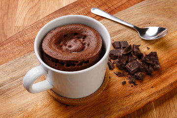 Delicious chocolate sponge pudding shot on a wooden board with a hand full of fudge pieces.