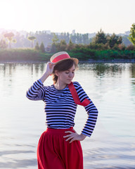 Girl in a straw hat near the water. Girl in a red skirt and a sailor suit