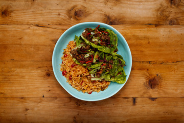 A bowl of succulent Spicy Beef Lettus Wraps on a bed of rice in a blue bowl on a wooden background