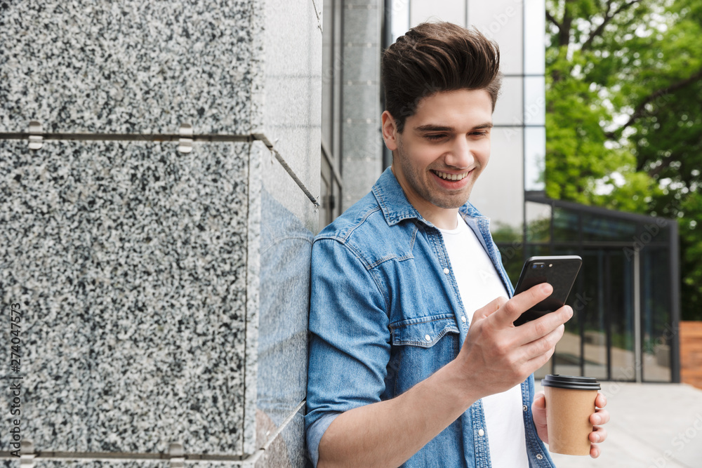 Poster happy young amazing man businessman posing outdoors outside walking chatting by mobile phone drinkin