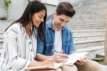 Image of happy couple talking and studying while sitting on bench near stairs outdoors