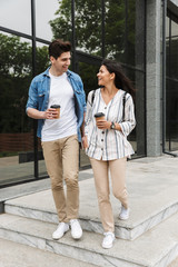 Image of caucasian couple drinking takeaway coffee while strolling through city street